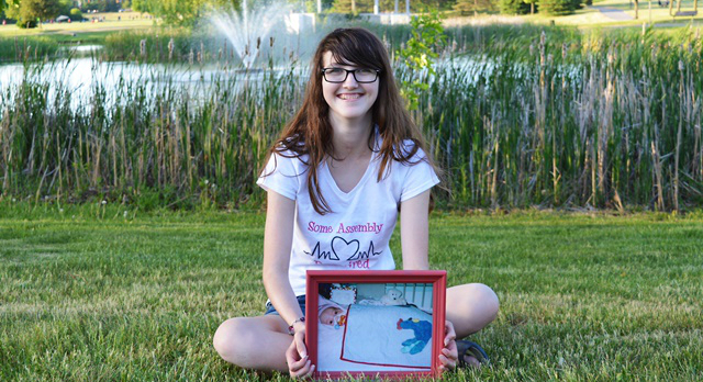 A teenage Abby MacMillan holds a picture of herself in the NICU