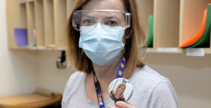 Staff wearing PPE and holding a button showing their face