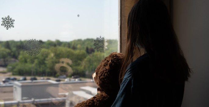 Silhouette of a youth looking out a window at CHEO, holding a teddy bear