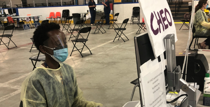 A CHEO staff member wearing PPE, sitting at a desk at the Brewer arena