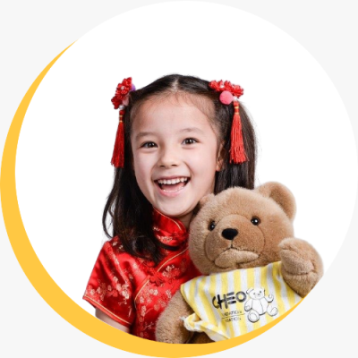 Photo of a young child in a kimono, holding a CHEO teddy bear and smiling at the camera