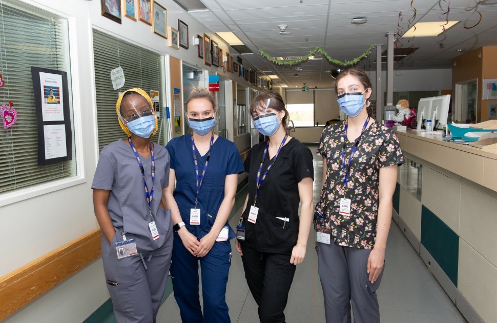 Four nurses smiling in their scrubs standing in a hallway