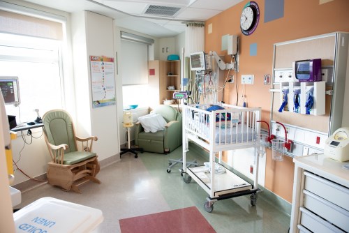 Photo of a NICU room, including a crib, rocking chair and clock on the wall.