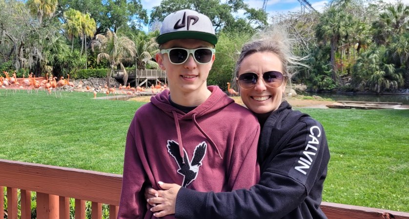 Christie Kopczyk hugging her son outside with flamingos in the background.