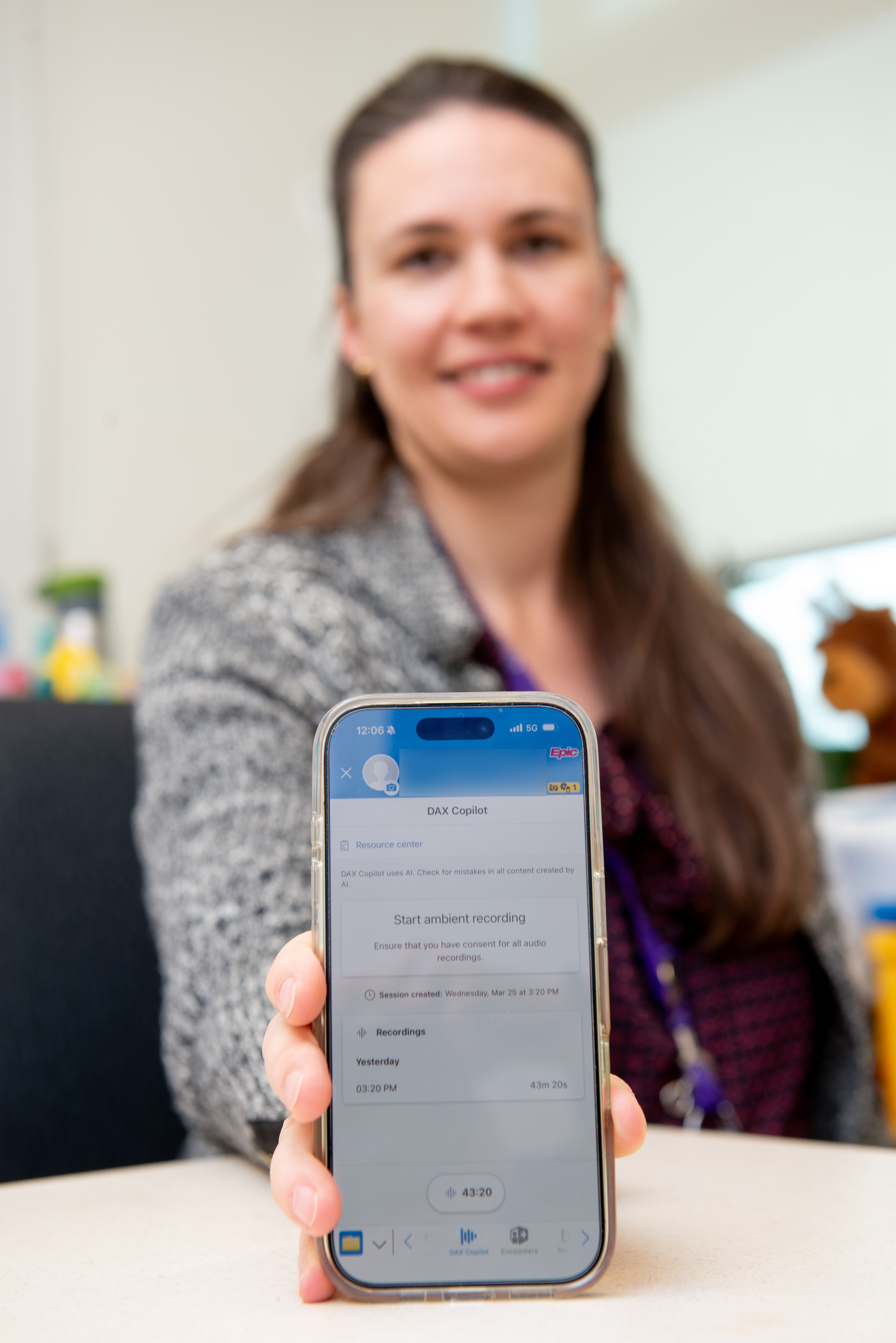 doctor holds phone in foreground with ai scribe app
