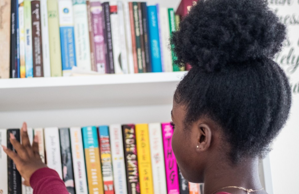 Young Black girl wearing a pink shirt standing in front of a bookshelf