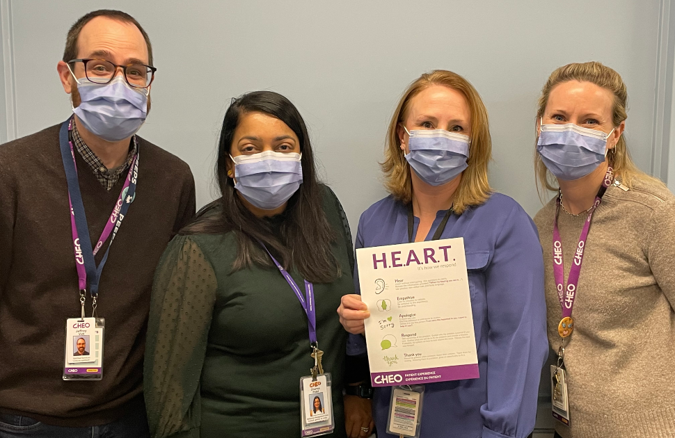 four members of patient experience team stand holding HEART steps on sign