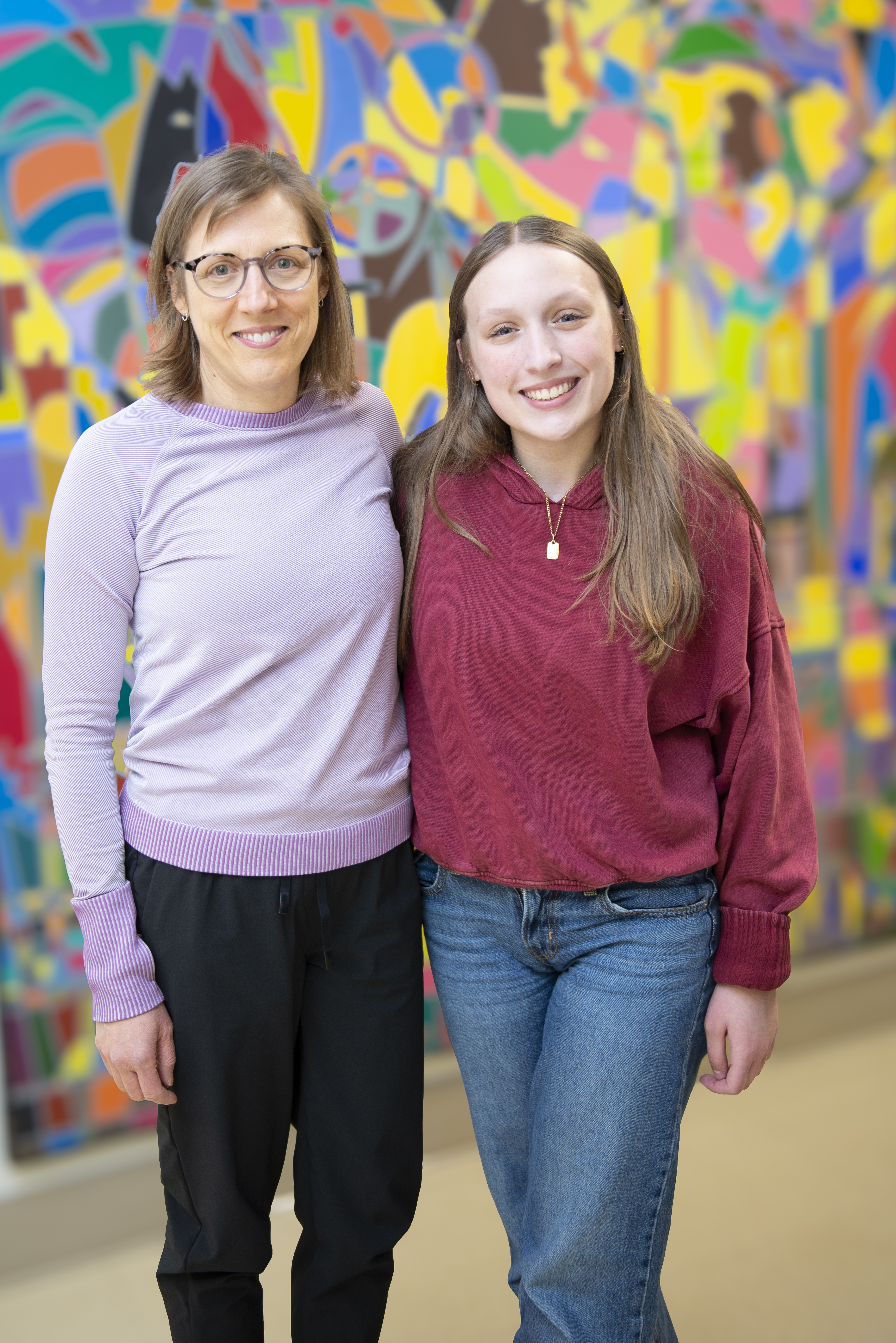 A woman and teenage girl post in front of a colourful wall.
