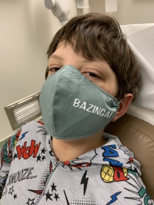 Young boy wearing a cloth mask that says "Bazinga" on it