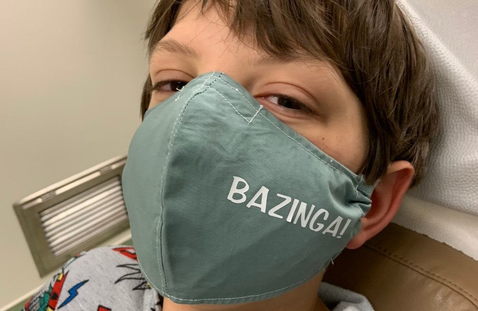 Young boy wearing a cloth mask that says "Bazinga" on it