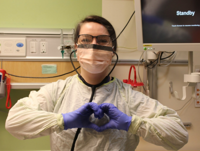Molly, a CHEO nurse, wearing PPE and smiling and making a heart with her hands