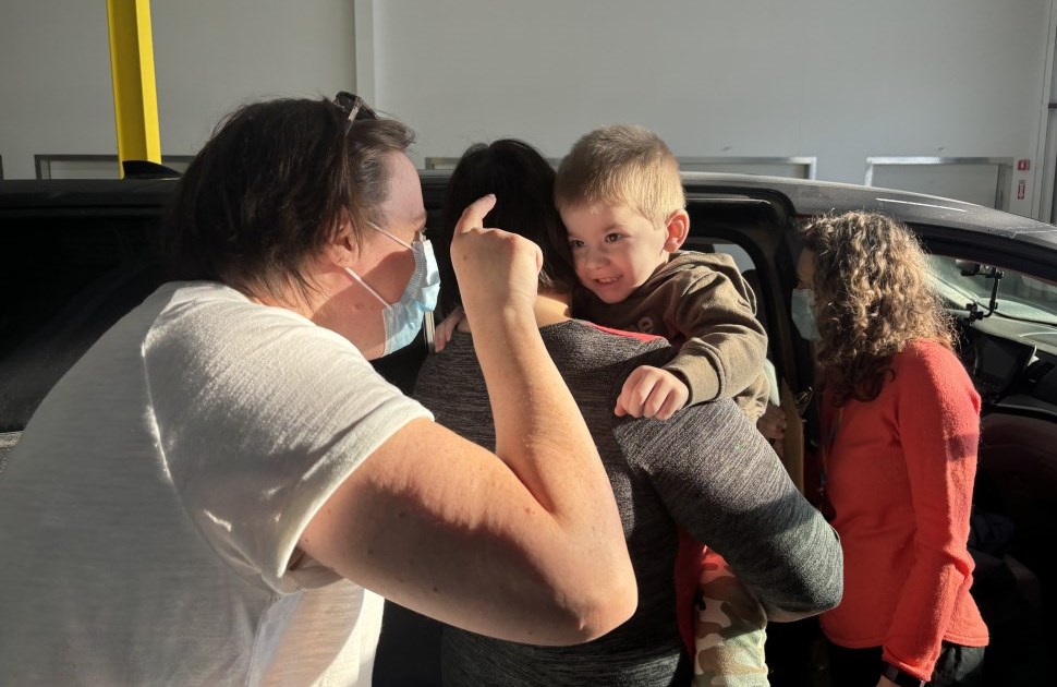 Photo of a child, parents  and Occupational Therapist standing by a car and car seat