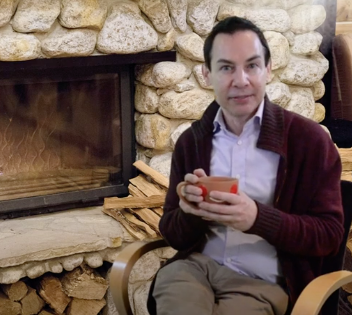 Alex Munter sitting in front of a fireplace, holding a mug