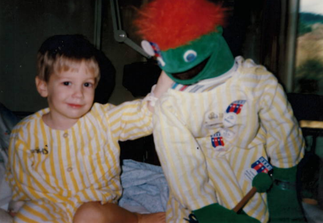 Strider, 3, beside a red-headed green puppet. Both Strider and the puppet wear yellow striped pyjamas.