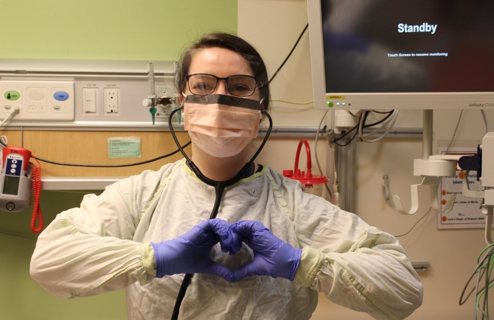 Person wearing full PPE making a heart shape with their hands.