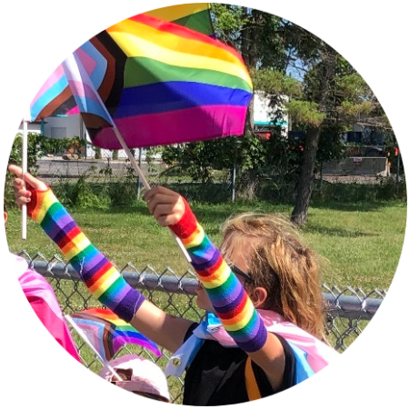 Ashe, waving Progress Pride flags and wearing a Trans pride flag