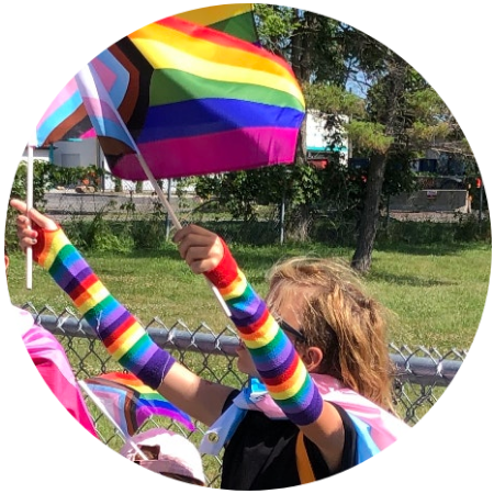 Ashe holding Progress Pride flags and wearing a trans flag