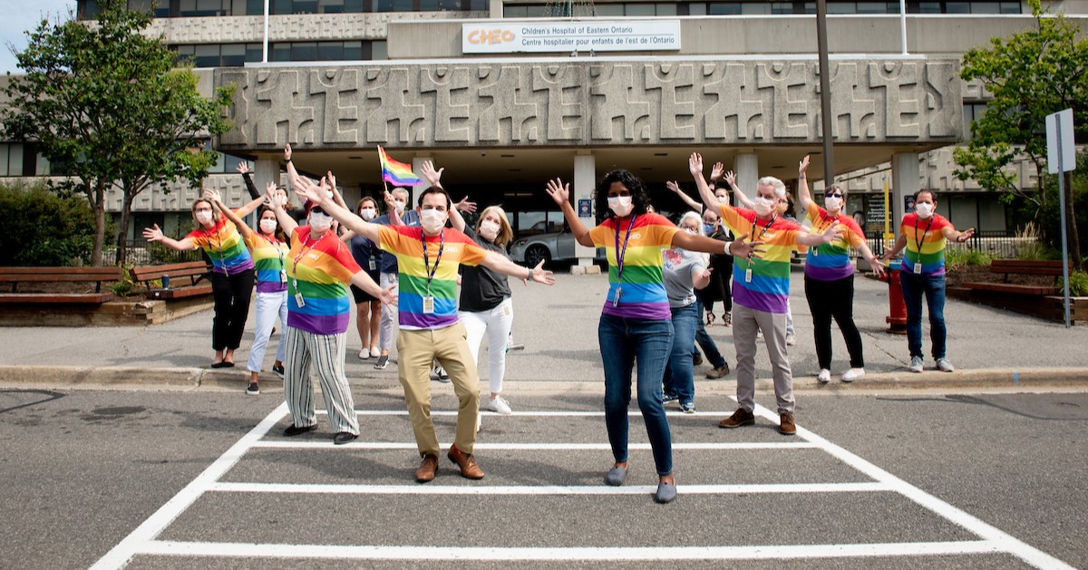 Group photo of CHEO staff and medical staff wearing rainbow t-shirts outside of the main entrance