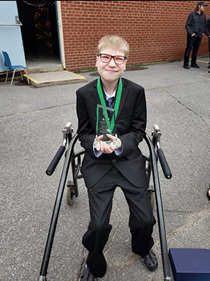 boy smiles while sitting in a wheelchair holding a trophy