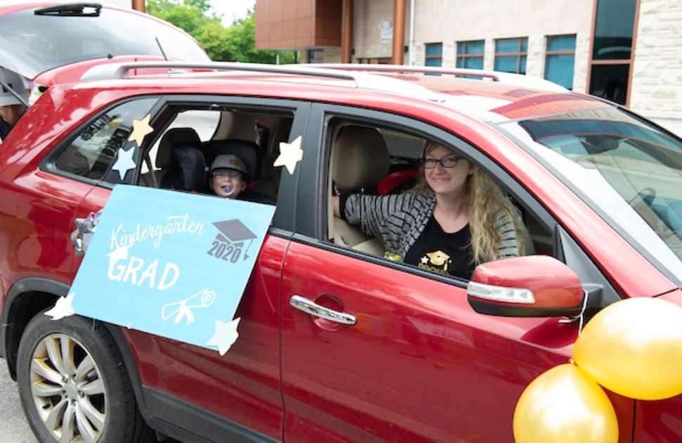 Little boy and mom in a car displaying a graduation sign