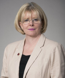 Ann Clancy. She has blond short hair, wear glasses and a beige blazer.