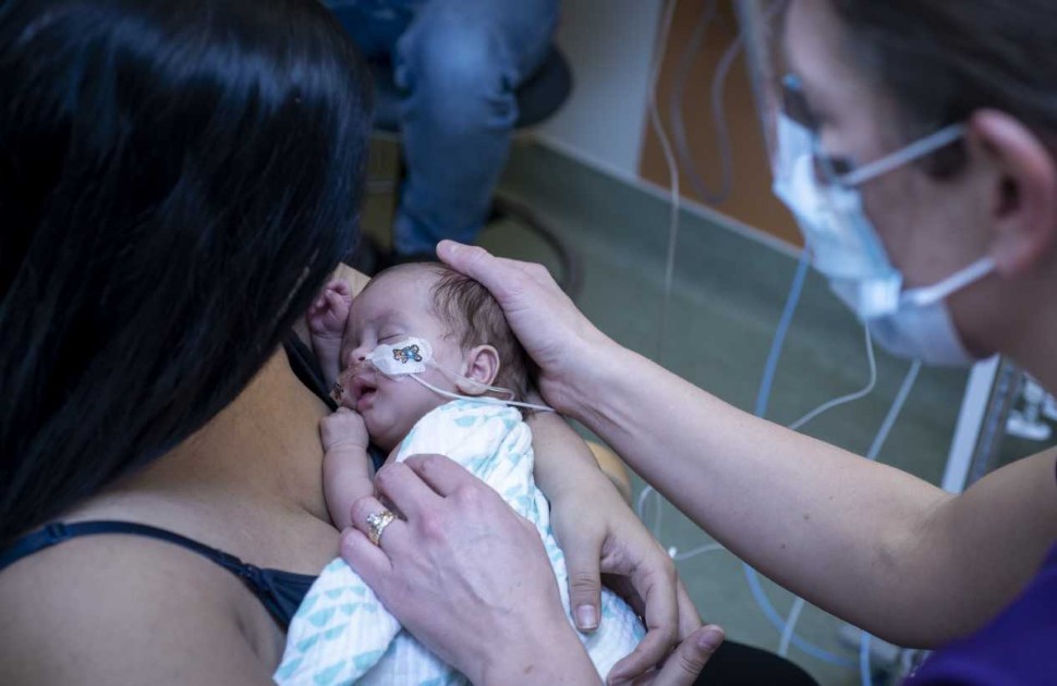 Mother holding her baby to her chest, with a CHEO staff member holding the baby's head