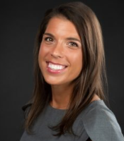 Photo of Melanie Buba, wearing a grey shirt and with brown hair, smiling at the camera