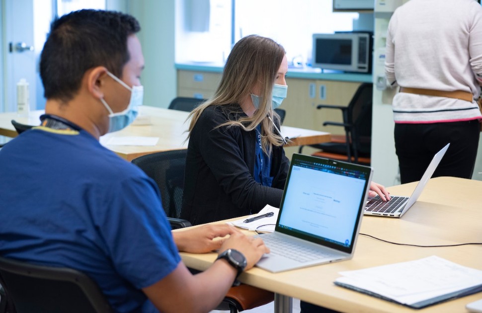 Staff in medical scrubs sitting in front of a laptop at a table