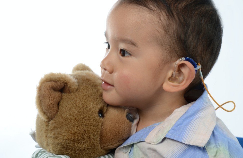 A child with a cochlear implant, holding a teddy bear