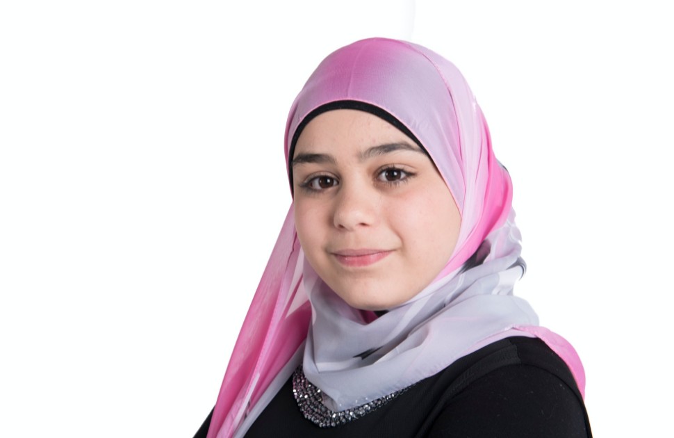 A young girl wearing a pink hijab, smiling at the camera